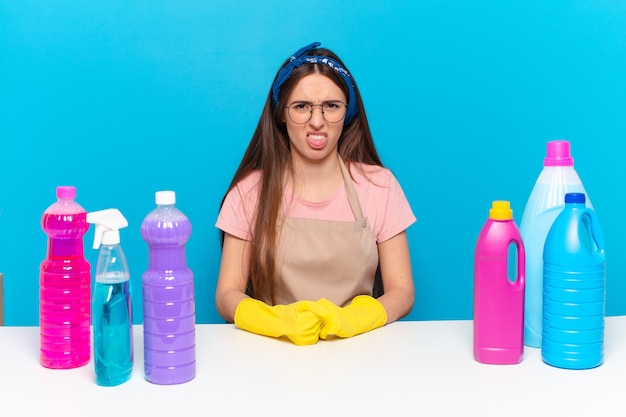 Young pretty house keeper feeling disgusted and irritated, sticking tongue out, disliking something nasty and yucky