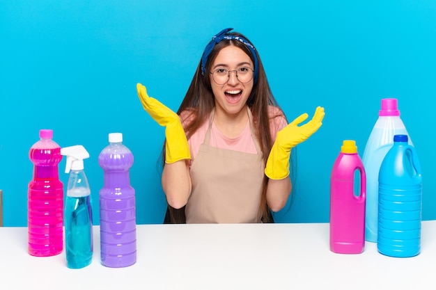 Young pretty house keeper feeling happy, excited, surprised or shocked, smiling and astonished at something unbelievable