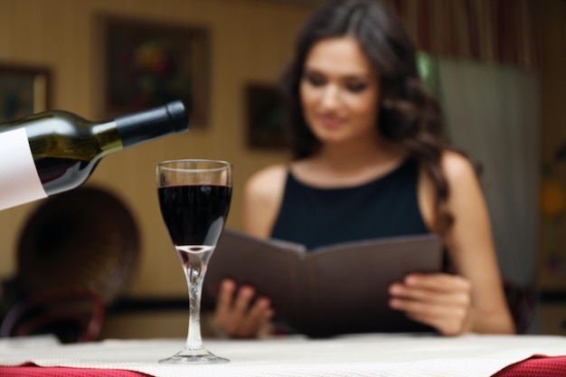 Young pretty lady at the restaurant. Waiter pouring wine in a glass