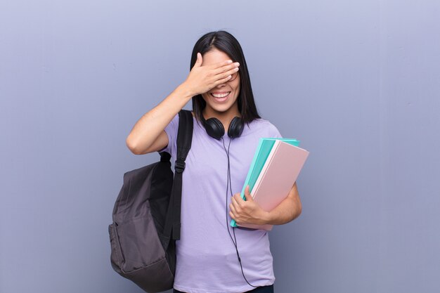 Young pretty latin student woman against gray wall