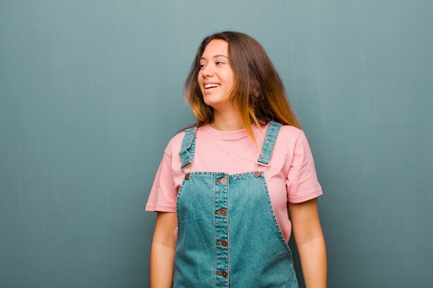 Young pretty latin woman feeling shocked, happy, amazed and surprised, looking to the side with open mouth against grunge wall