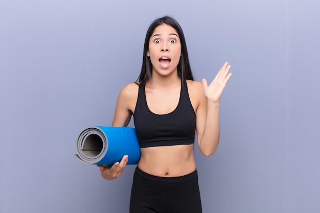 Young pretty latin woman with a yoga mat against cement wall