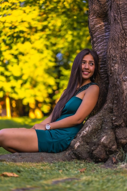 A young pretty Latina brunette with long straight hair leaning against a tree