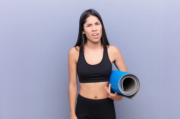 Young pretty lating woman with a yoga mat against cement wall