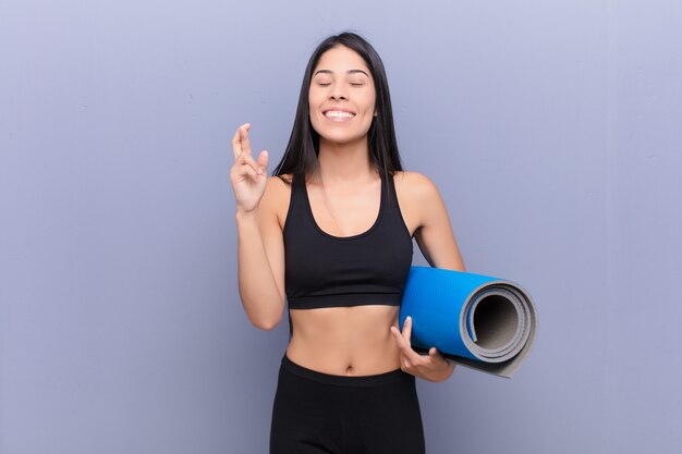 Young pretty lating woman with a yoga mat against cement wall