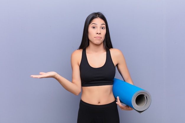 Young pretty lating woman with a yoga mat against cement wall