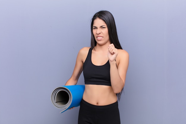 Young pretty lating woman with a yoga mat against cement wall