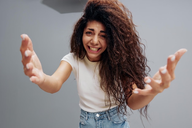 Young pretty laughing cheerful friendly latin woman 20s afro\
long hair in casual white shirt stretch hands isolated on pastel\
gray color background studio portrait wide angle view copy\
space