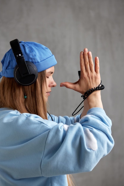 Una giovane ragazza dj dai capelli lunghi con un cappello divertente maglione blu e le cuffie ha piegato le mani in ap