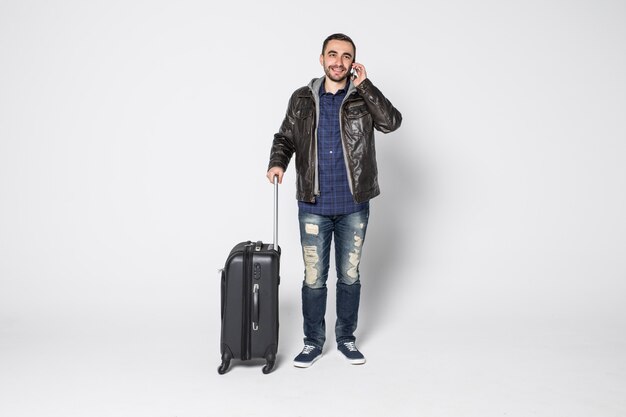 Young pretty man with suitcase talking on the phone isolated over white background Y