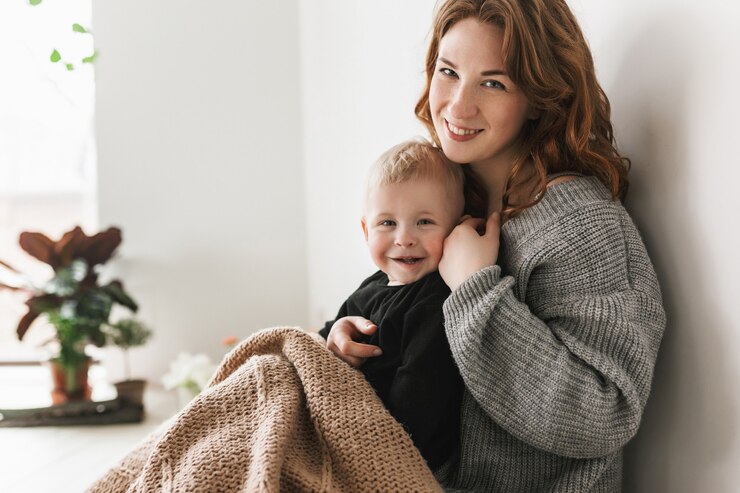 Young pretty mom with red hair in knitted sweater sitting on floor, holding her little handsome son