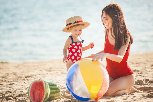 ビーチで彼女の小さなかわいい娘と遊ぶ若いかなり母親。海岸で彼女の子供を楽しんでママを愛する