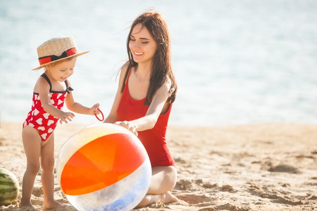 Giovane madre graziosa che gioca con la sua piccola figlia sveglia alla spiaggia. amorevole mamma divertirsi con il suo bambino in riva al mare