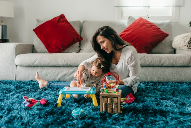 Young pretty mother plays with her daughter on the floor