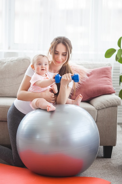 Young pretty mother working out with her little child at home