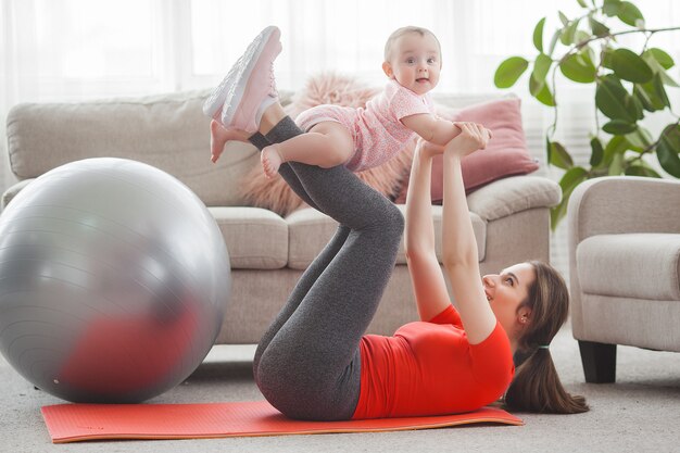 Young pretty mother working out with her little child at home