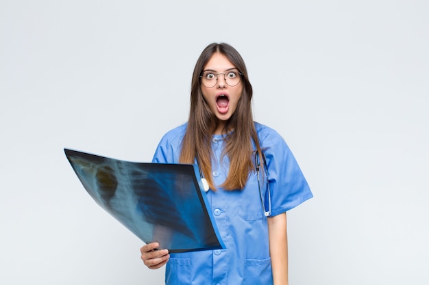 Young pretty nurse looking very shocked or surprised, staring with open mouth saying wow