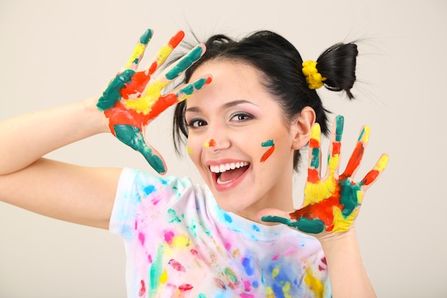 Young pretty painter with hands in paint on gray background