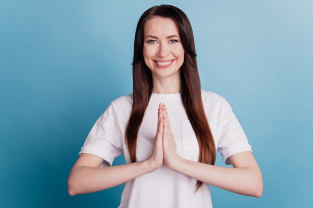 Young pretty pleaded woman with hands folded in prayer gesture isolated on blue background