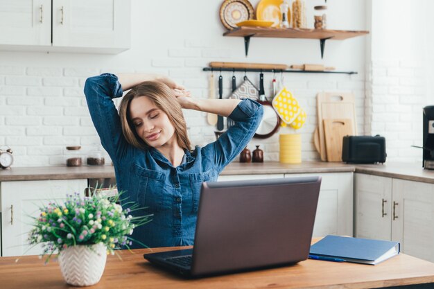 Young pretty pregnant freelancer girl works at home in the kitchen in self-isolation mode in quarantine and does a warm-up from fatigue