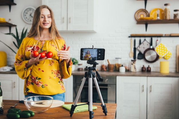 写真 若いかなり妊娠中の女の子のブロガーがスマートフォンのカメラでサラダレシピのビデオを撮影します