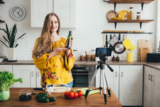 Young pretty pregnant girl blogger shoots a video of a salad recipe on a smartphone camera