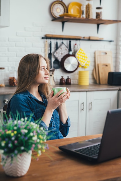 Young pretty pregnant girl works at home in self-isolation mode in quarantine and takes a break for rest with coffee