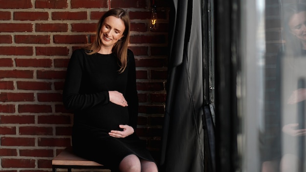 Young pretty pregnant woman in black dress in studio - loft interior