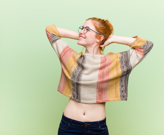 Photo young pretty red head woman smiling and feeling relaxed, satisfied and carefree, laughing positively and chilling against green wall