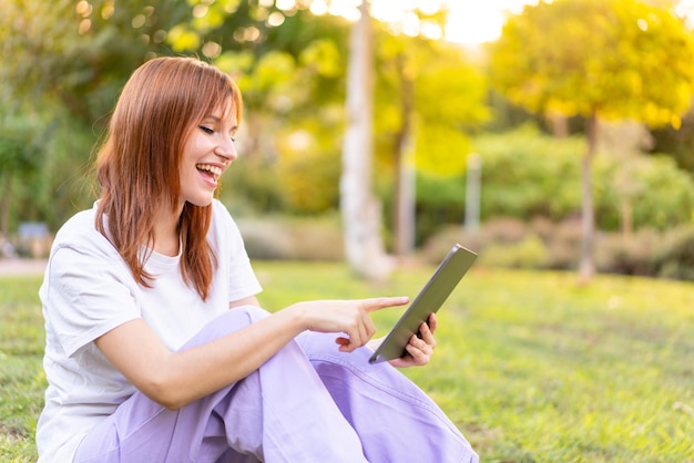 Young pretty redhead woman at outdoors holding a tablet