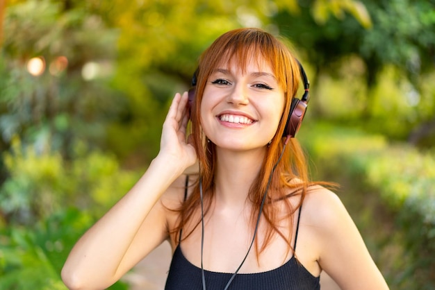 Young pretty redhead woman at outdoors listening music