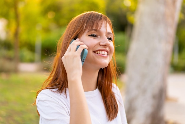 Young pretty redhead woman at outdoors using mobile phone with happy expression