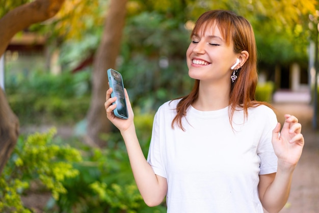 Young pretty redhead woman at outdoors using mobile phone