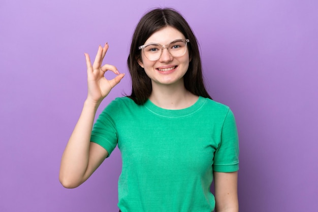 眼鏡とOKサインをしている紫色の背景に分離された若いきれいなロシアの女性