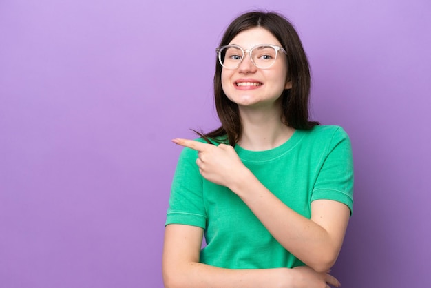 Young pretty russian woman isolated on purple background with glasses and pointing side