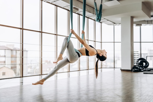 Young pretty slim body fitness girl practicing fly yoga in the gym.