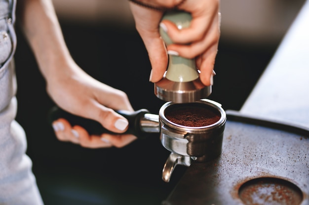 カジュアルな服を着たかなりスリムな若い女の子が、モダンなコーヒーショップでコーヒーを作っています。それはプロセスに焦点を合わせています。 。