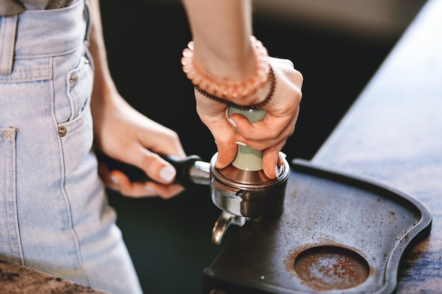 캐주얼 복장을 한 젊고 날씬한 소녀가 현대적인 커피숍에서 커피를 요리하고 있습니다. 과정에 중점을 두고 있습니다. .