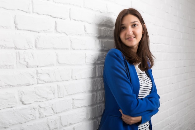 A young pretty smiling girl against a white loftstyle brick wall She looks at the viewer Copy space