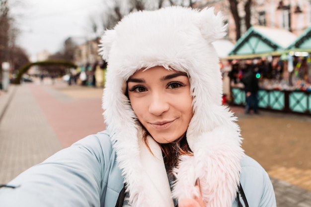 Young pretty smiling woman celebrating dressed warm jacket and woven woolen hat, taking sealfie