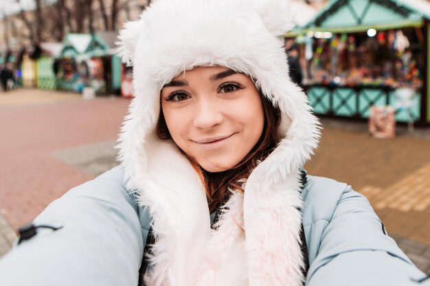 Young pretty smiling woman celebrating dressed warm jacket and woven woolen hat, taking sealfie