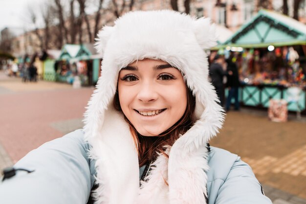 Young pretty smiling woman celebrating dressed warm jacket and woven woolen hat, taking sealfie