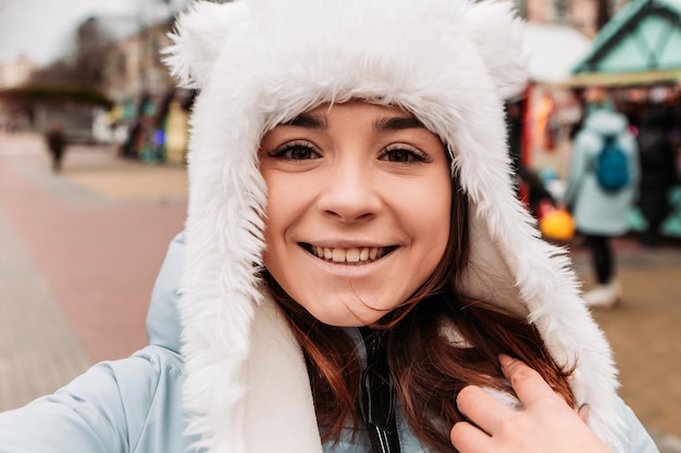 Young pretty smiling woman celebrating dressed warm jacket and woven woolen hat, taking sealfie