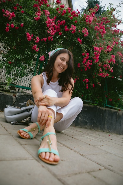 Young pretty smiling woman near blooming red roses bush copy space