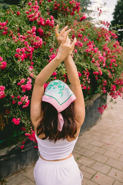 Young pretty smiling woman near blooming red roses bush copy space