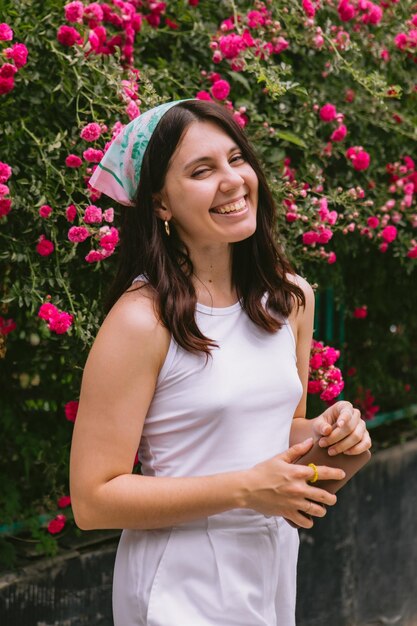 Young pretty smiling woman near blooming red roses bush copy space