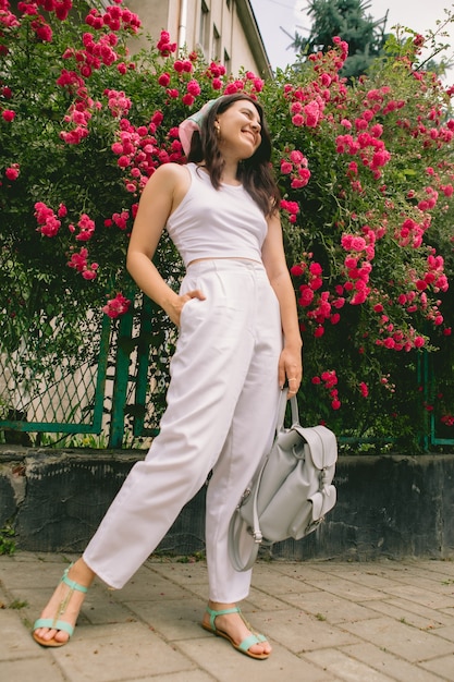 Young pretty smiling woman near blooming red roses bush copy space