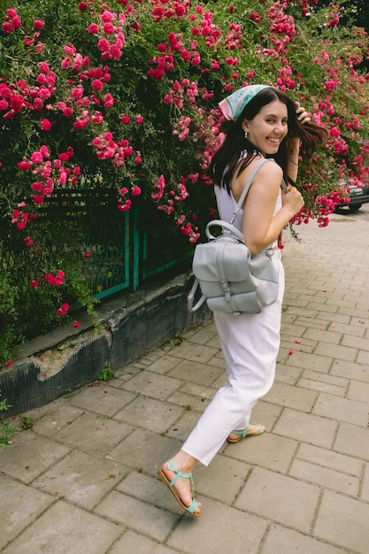 Young pretty smiling woman near blooming red roses bush copy space