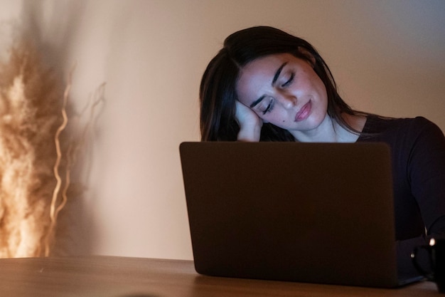 Young pretty smiling woman using laptop in home at night Happy girl looking at computer Cheerful people sitting at desk in living room Concept of enterprising telecommuting and hardworking person