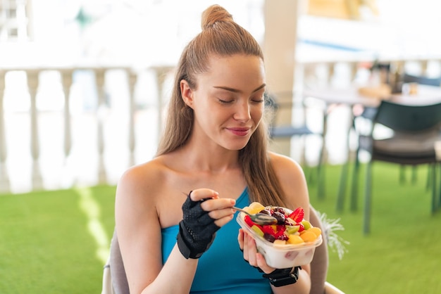 Young pretty sport girl holding a bowl of fruit at outdoors